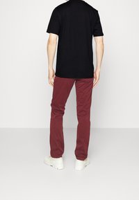 Camiseta negra de manga corta, pantalones rojos y zapatillas blancas. Tejido suave, ajuste estándar y diseño básico sin patrones ni logotipos visibles.