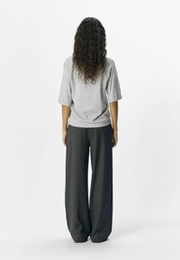 Grå oversized t-shirt med korte ærmer, parret med mørke, vide bukser. Stoffet ser blødt ud med en glat tekstur.