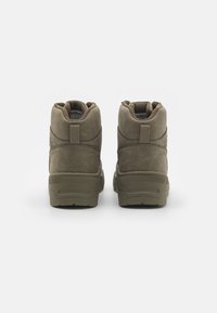 Botas de tobillo de ante marrón con cuello acolchado, que presentan un panel trasero texturizado y una suela de goma, diseñadas para la durabilidad y la comodidad.
