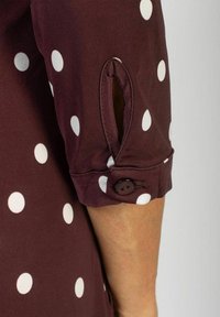 Koszula w kolorze burgundu w białe groszki, z podwiniętymi rękawami i guzikami na mankiecie, o gładkiej fakturze.