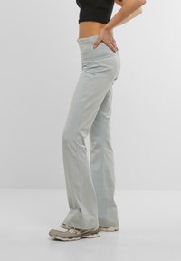 Pantaloni svasati grigio chiaro con vita alta, realizzati in materiale elasticizzato. Il modello indossa sneakers grigie e beige. Design semplice e lineare.