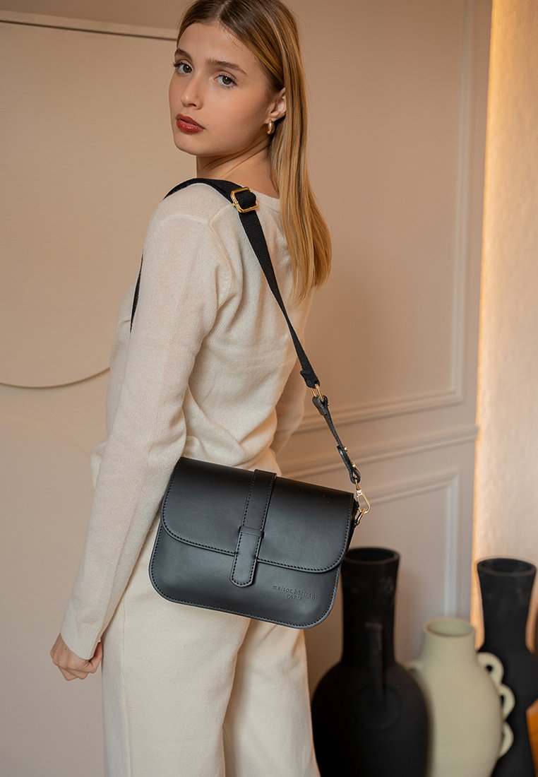 Zwarte leren handtas met een flap sluiting, verstelbare strap en subtiele branding. Gladde textuur en rechthoekige vorm, te dragen als crossbody.