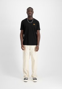 Svart t-skjorte med korte ermer og oransje logo, kombinert med beige cargo-bukser og svart-hvite sneakers. Enkelt design, uformell passform.