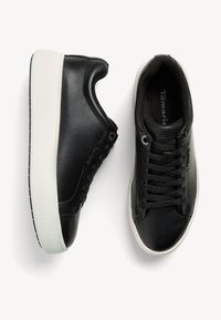 Sneaker in pelle nera con finitura liscia e punta rotonda. Presentano lacci in tessuto, suola in gomma bianca a contrasto e dettaglio del logo sul lato.