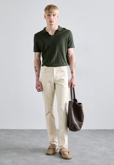 Polo shirt verde oliva a maniche corte, pantaloni dritti color avorio, borsa in pelle marrone, scarpe beige slip-on; look minimalista e casual.