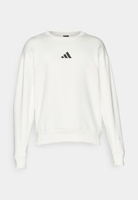 Balts krekls ar apaļu kakla izgriezumu, plašām piedurknēm, izgatavots no kokvilnas, ar nelielu melnu Adidas logo uz krūškurvja.