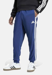 Pantalones deportivos color azul marino con franjas laterales blancas, hechos de una tela ligera, que cuentan con una cinturilla elástica y un ajuste relajado.