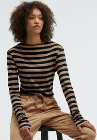 Gestreiftes Langarmoberteil in Schwarz und Beige. Weicher, dehnbarer Stoff mit rundem Ausschnitt und enganliegenden Ärmeln. Kombiniert mit beigen Jogginghosen mit Kordelzug.