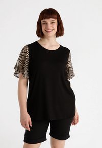 T-shirt nera con maniche corte a campana con stampa zebra. Tessuto morbido e scollatura rotonda. Abbinata a pantaloni corti neri arrotolati.