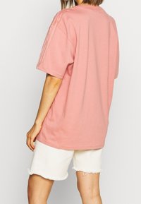 Rosa bomullströja med korta ärmar och tre ränder på axlarna, kombinerad med vita fransade shorts. Enkel, avslappnad passform.