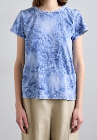 Camiseta de algodón azul con efecto tie-dye, de cuello redondo, mangas cortas y corte relajado. Presenta una textura sutil y un dobladillo cosido.