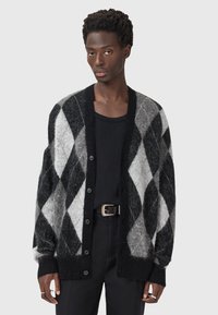 Un cardigan à motif argyle noir et gris en tricot doux et texturé. Il présente un devant à boutons et des poignets et un ourlet côtelés.