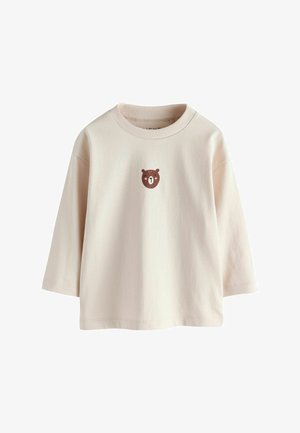 Langærmet babyshirt i cremefarve med lille, centreret brun bjørneansigt på brystet og ribstrikket rund halsudskæring.
