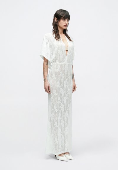 Pikk, läbipaistev valge rüü lillemustriga, laiad varrukad, sügav V-kaelus, voolava disainiga, koos valgete teravate kontsakingadega.