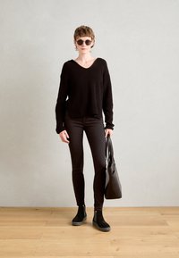 Schwarzer oversized Rippstrickpullover, dunkle Jeans, schwarze Wildleder-Stiefeletten und eine schwarze Tote-Tasche; modernes, minimalistisches Design, strukturierte Materialien.