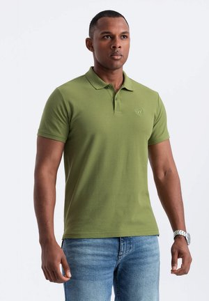 Camisa polo verde hecha de una mezcla de algodón, con cuello clásico, mangas cortas y un pequeño logotipo en el lado izquierdo del pecho. Se lleva con pantalones vaqueros azules.