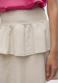Gonna beige chiara con una vita arricciata e un orlo a strati e ondulato. Tessuto texturizzato con un aspetto morbido e leggermente stropicciato.