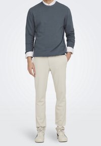 Felpa blu scuro, pantaloni beige, indossati con una camicia a righe con colletto. Abbigliamento casual con una vestibilità comoda e dettagli minimi.