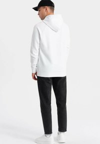 Un sweat à capuche blanc avec une poche kangourou, un ourlet côtelé et une capuche avec cordon, associé à un jean noir et des baskets blanches.