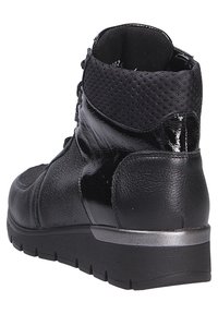 Bottine noire avec un mélange de cuir lisse et texturé, un col rembourré et une semelle en caoutchouc robuste avec un petit accent métallique.