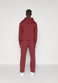 Mørkerød hoodie og matchende joggers lavet af blødt materiale. Hoodien har en snor i hætten, mens bukserne har et tapered design.