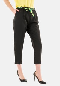 Pantaloni neri con vestibilità ampia, dotati di una cintura a strisce verdi e gialle, orli con risvolto e tasche laterali. Indossati con tacchi alti neri.