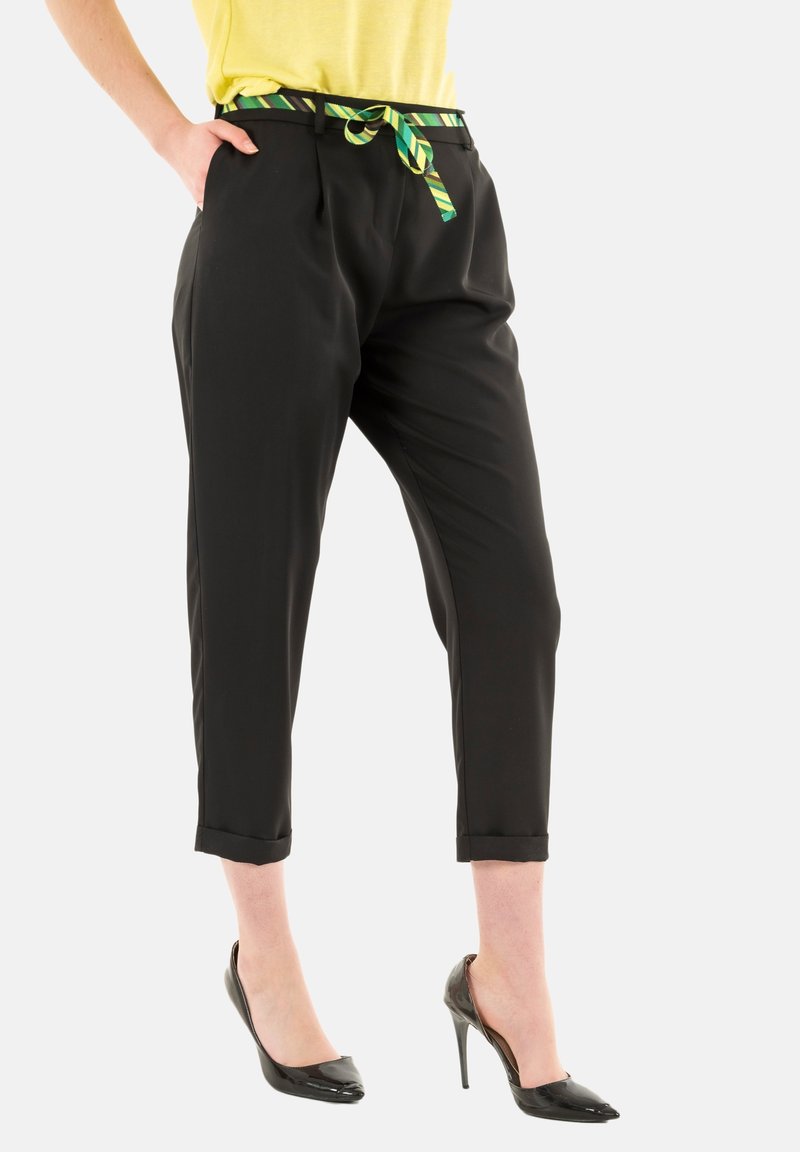 Pantaloni neri con vestibilità ampia, dotati di una cintura a strisce verdi e gialle, orli con risvolto e tasche laterali. Indossati con tacchi alti neri.