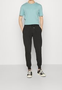 Ljusblå t-shirt med kort ärm, svarta joggerbyxor med elastiska muddar och dragsko, kombinerat med svarta och vita sneakers.