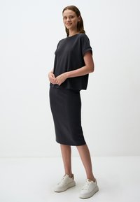 Twee-delig outfit in donkergrijze stof; kortmouwtop met opgerolde mouwen, gecombineerd met een rok tot de knie. Geaccentueerd met witte sneakers.