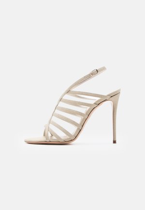 Smėlio spalvos aukštakulnė basutė su keliais horizontaliais dirželiais, kulkšnies dirželiu su sagtimi ir liesu stiletto kulniuku ant balto fono.