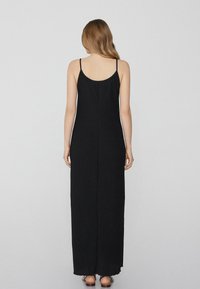 Schwarzes Maxikleid mit dünnen Trägern, einem runden Rücken-Halsausschnitt, einer geraden Silhouette und einem fransigen Saum am Boden. Glatte Stofftextur.