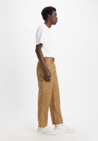 Camiseta ligera de algodón blanco combinada con pantalones cargo en color beige con múltiples bolsillos y un corte relajado; llevada con zapatillas blancas.