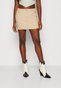 Beige denim minikjol med framfickor, kontrasterande sömmar och en figurnära midja, tillsammans med vita och svarta västerländska ankelstövlar.