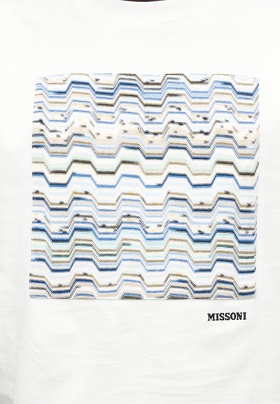 Λευκό ύφασμα με ορθογώνιο πολύχρωμο ζιγκ ζαγκ μοτίβο σε μπλε, μπεζ και μαύρους τόνους, με κεντημένο κάτω το κείμενο «MISSONI».