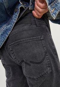 Černé džíny z denimu s mírnou texturou, se designem zadní kapsy a koženou značkovou nášivkou viditelnou poblíž pásku.