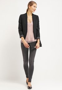 Fekete blézer, rózsaszín csipkeborítású topp, testhez simuló szürke farmernadrág és fekete hegyes orrú balerina cipő. A modell egy fekete clutch-ot tart. Sima szövet textúrák az összeállításon.
