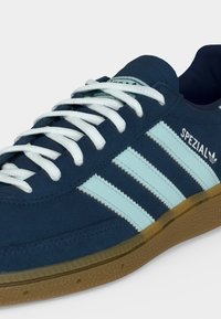 Baskets Adidas Spezial bleu foncé avec des rayures bleu clair, des lacets blancs et une semelle en gomme, montrées en gros plan de profil.