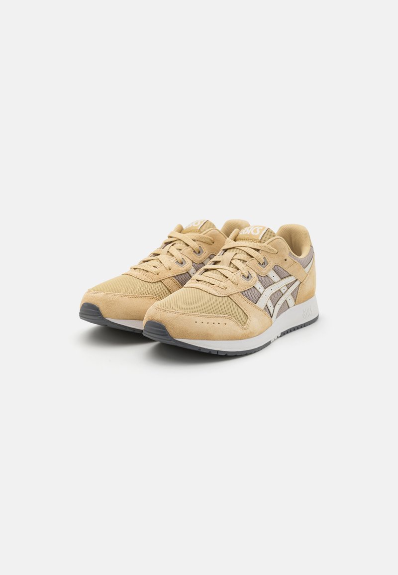 Zapatillas de ante y malla en color beige con un diseño de cordones, que presentan detalles en blanco y gris y una suela de goma con surcos para mayor tracción.