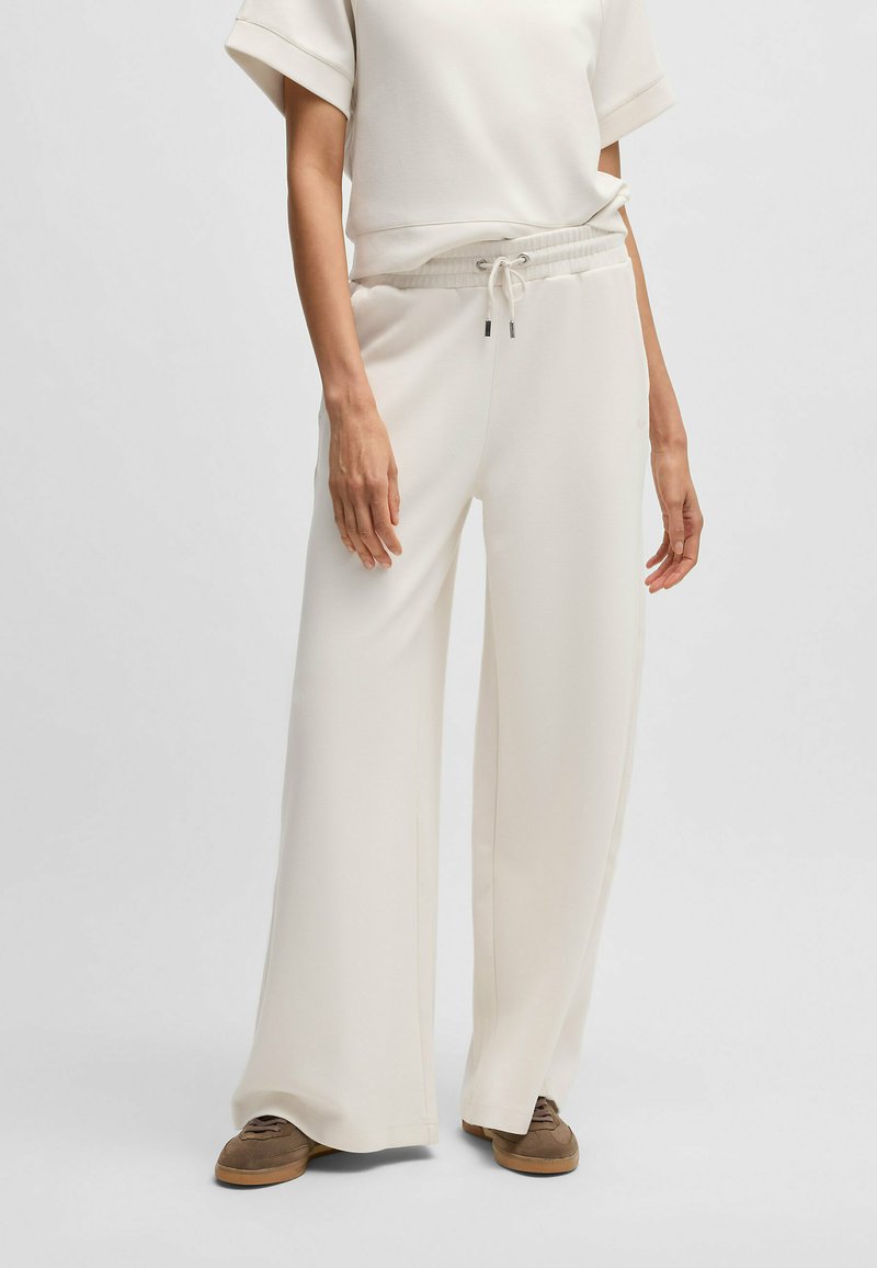 Wide-leg, cream-colored pants with a drawstring waist and soft texture, paired with a matching top, set against a plain background.