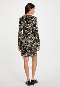 Langärmliges Kleid mit einem schwarz-beigen Zebra-Muster. Figurbetonter Schnitt mit leicht ausgestelltem Saum, gefertigt aus strukturiertem Stoff.