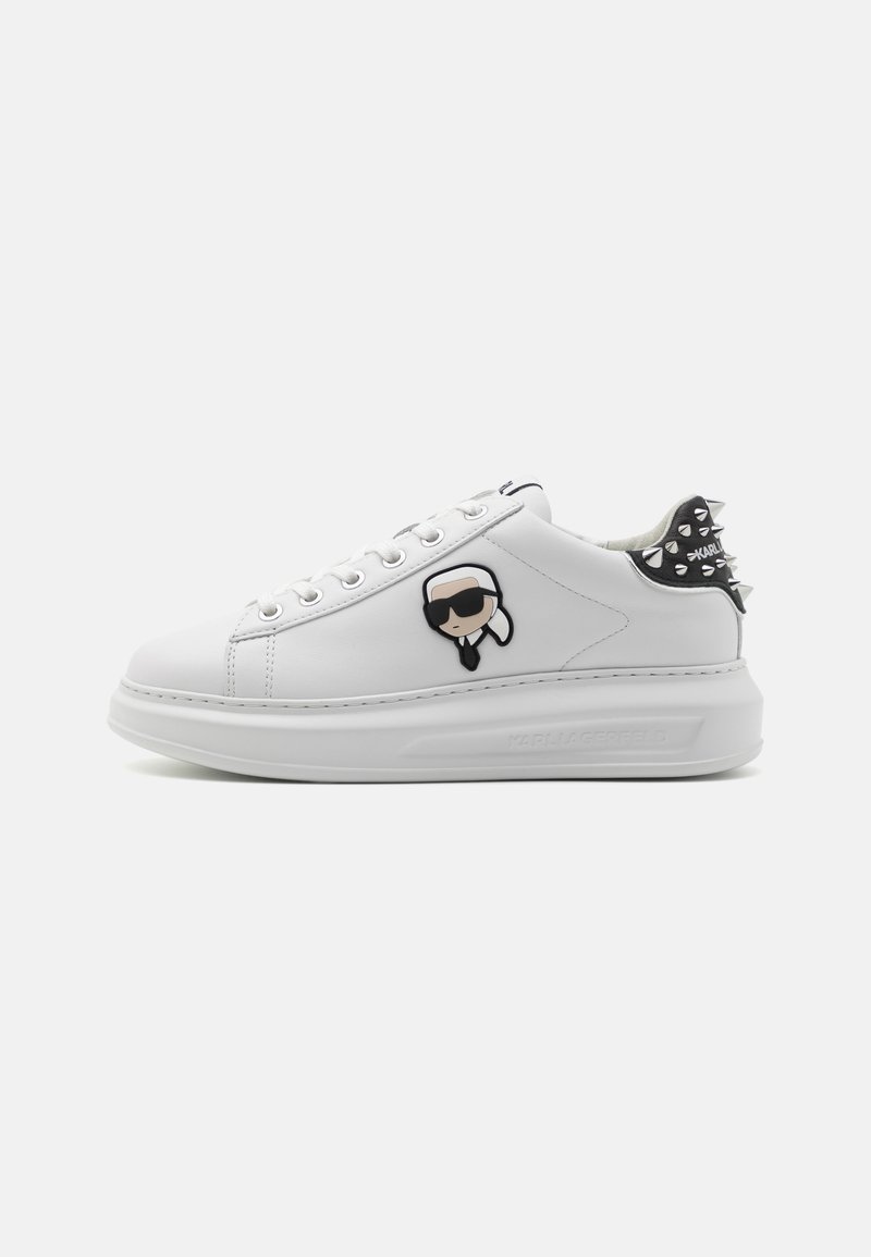 White sneaker with thick sole, embroidered cartoon face with sunglasses on side, and black heel with silver spikes.