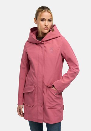 Vrouw draagt een lange roze jas met kap en twee grote voorzakken, staand met één hand in een zak tegen een effen achtergrond.