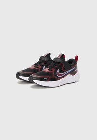 Une paire de baskets Nike noires et rouges avec un swoosh bleu, des bandes velcro et des semelles blanches sur un fond clair.