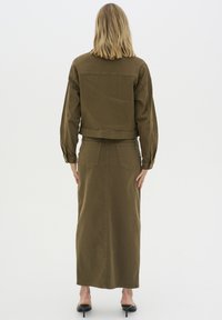 Giacca di denim khaki e lunga gonna, entrambe con una texture liscia. La giacca presenta un design cropped, polsini con bottoni e tasche posteriori.