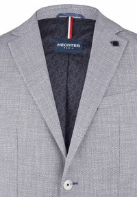 Hellgrauer Blazer aus strukturiertem Stoff, mit einem einzelnen Knopfverschluss und marineblauer gemusterter Fütterung sowie einem Markenetikett.