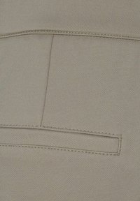 Ljus beige tyg med en fin textur, som har en horisontell ficköppning med rena stygn längs kanterna.