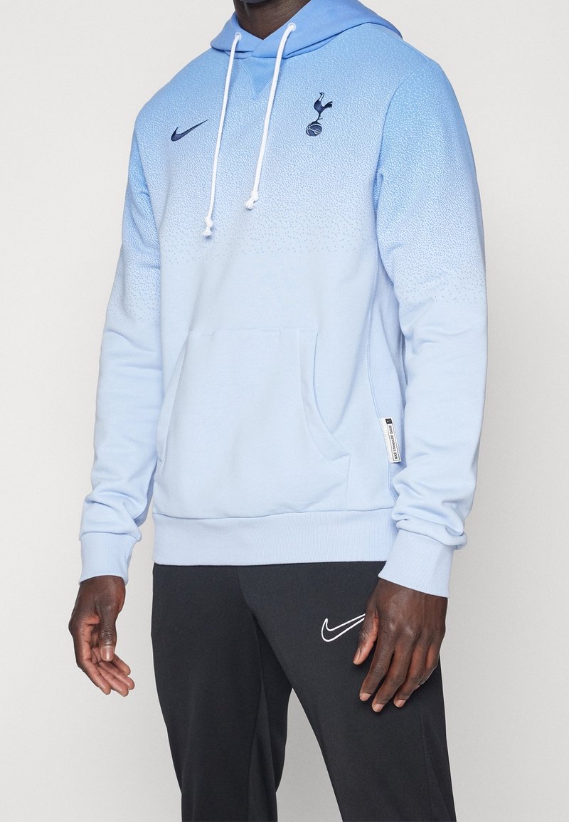 Felpa blu chiaro con design a gradiente, logo Nike ed emblema del Tottenham Hotspur. Presenta una tasca frontale e cappuccio con coulisse. Tessuto morbido.