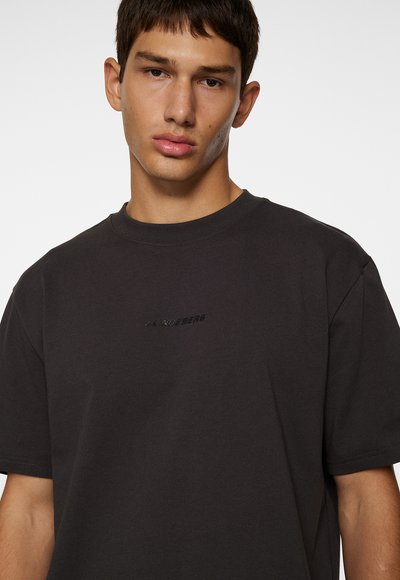 Svart bomullströja med rundad halsringning, som har en subtil präglad logotyp i mitten, korta ärmar och en avslappnad passform.