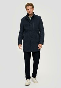 Donkerblauwe wollen mix jas met een knoopsluiting aan de voorkant, zijzakken, een hoge kraag en een ritszak op de borst, gecombineerd met marineblauwe cargobroeken en sneakers.