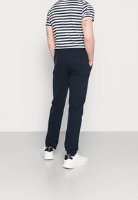 Marineblauwe, lichte broeken met een rechte pasvorm, voorzien van twee zijzakken en een achterzak. Gemaakt in combinatie met een gestreept, kortmouwen t-shirt en witte sneakers.